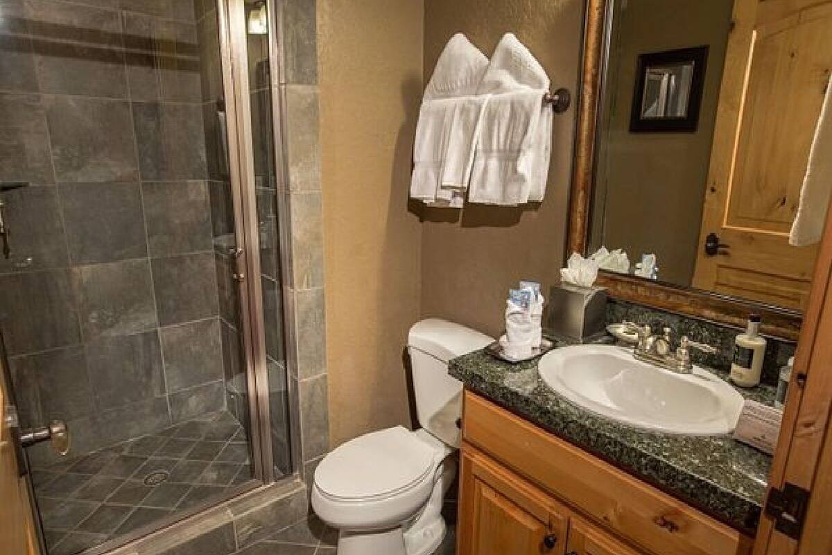 Un baño con ducha de vidrio, inodoro, lavamanos con espejo y perchero para toallas.