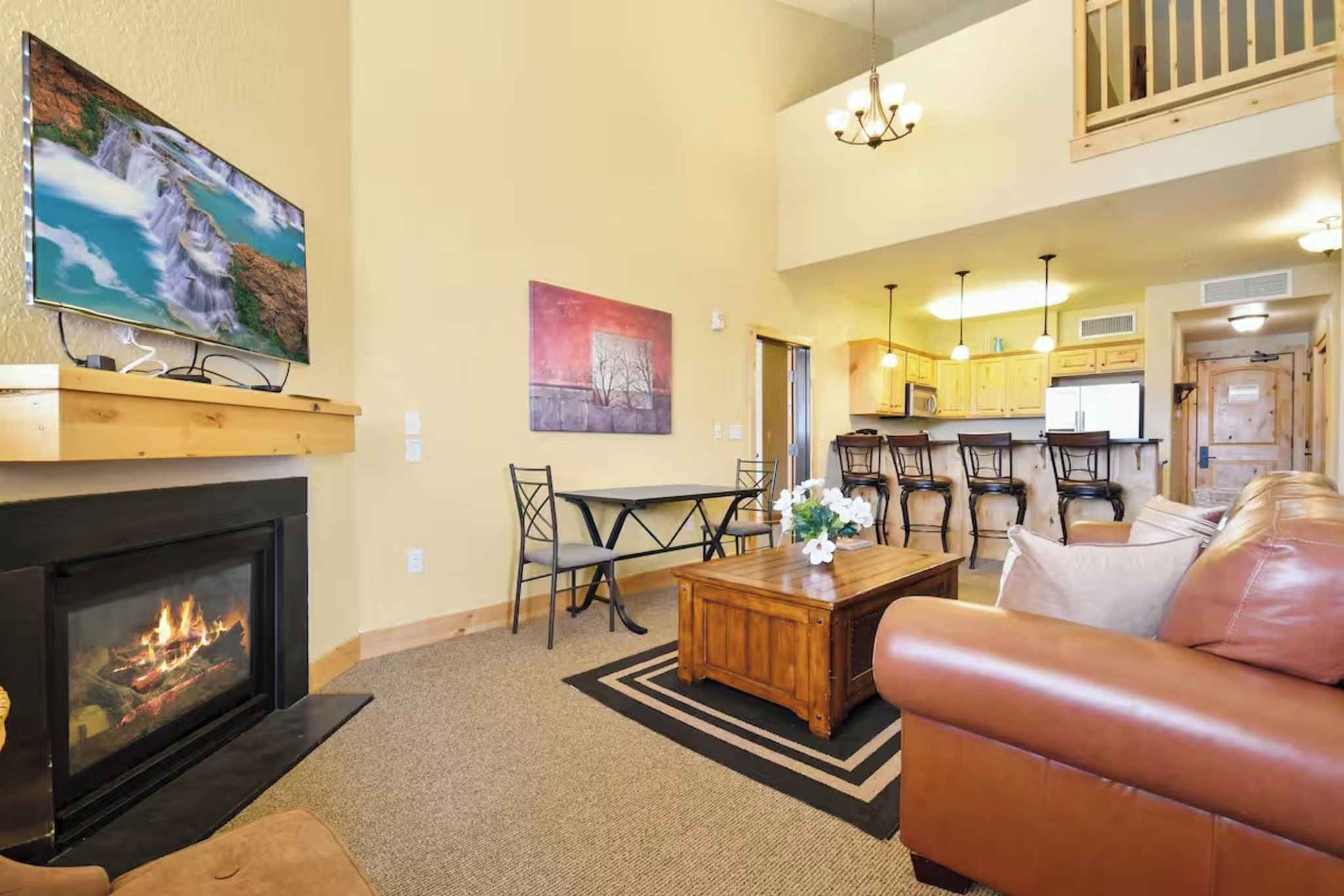A living room with a fireplace, a television, a dining area with bar stools, and a kitchen in the background.