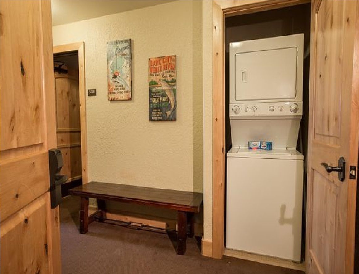 A laundry room with a bench, a white washing machine, and two posters on the wall.