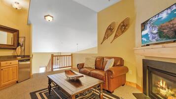 A living room with a fireplace, a sofa, a coffee table, and a television mounted above the fireplace.