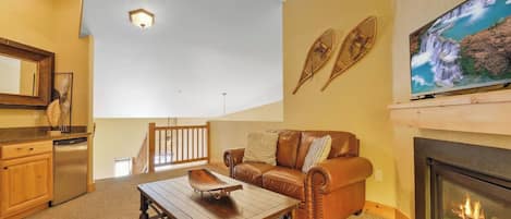 A living room with a fireplace, a sofa, a coffee table, and a television mounted above the fireplace.