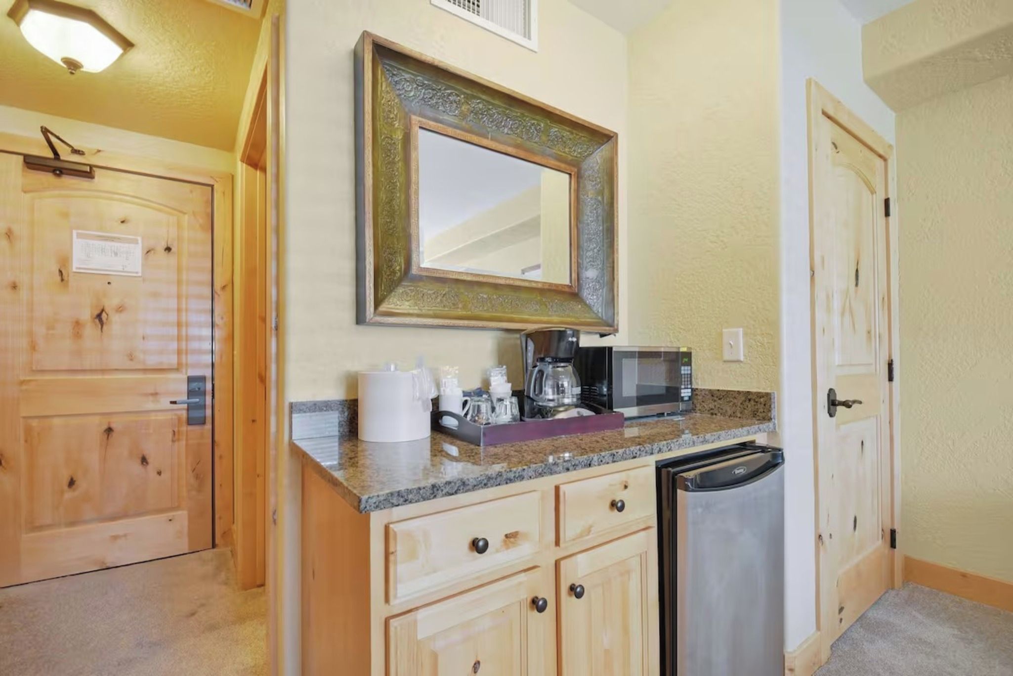 A compact kitchen with wooden cabinets, a microwave, a coffee maker, and a dishwasher.
