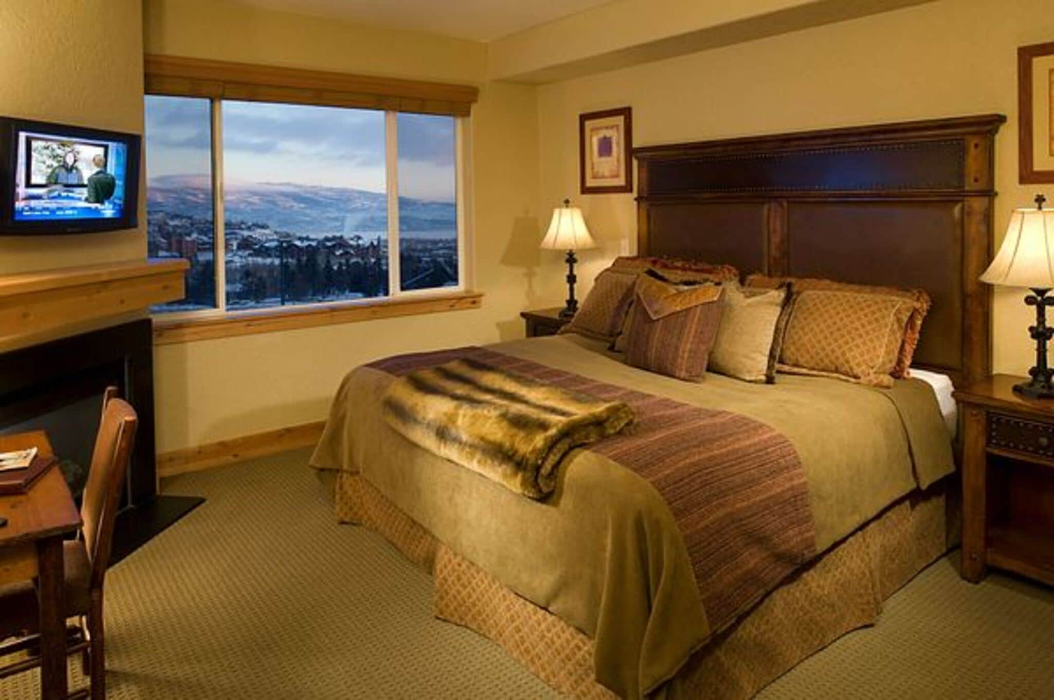 A hotel room with a large bed, a desk with a chair, a television, and a window with a view.