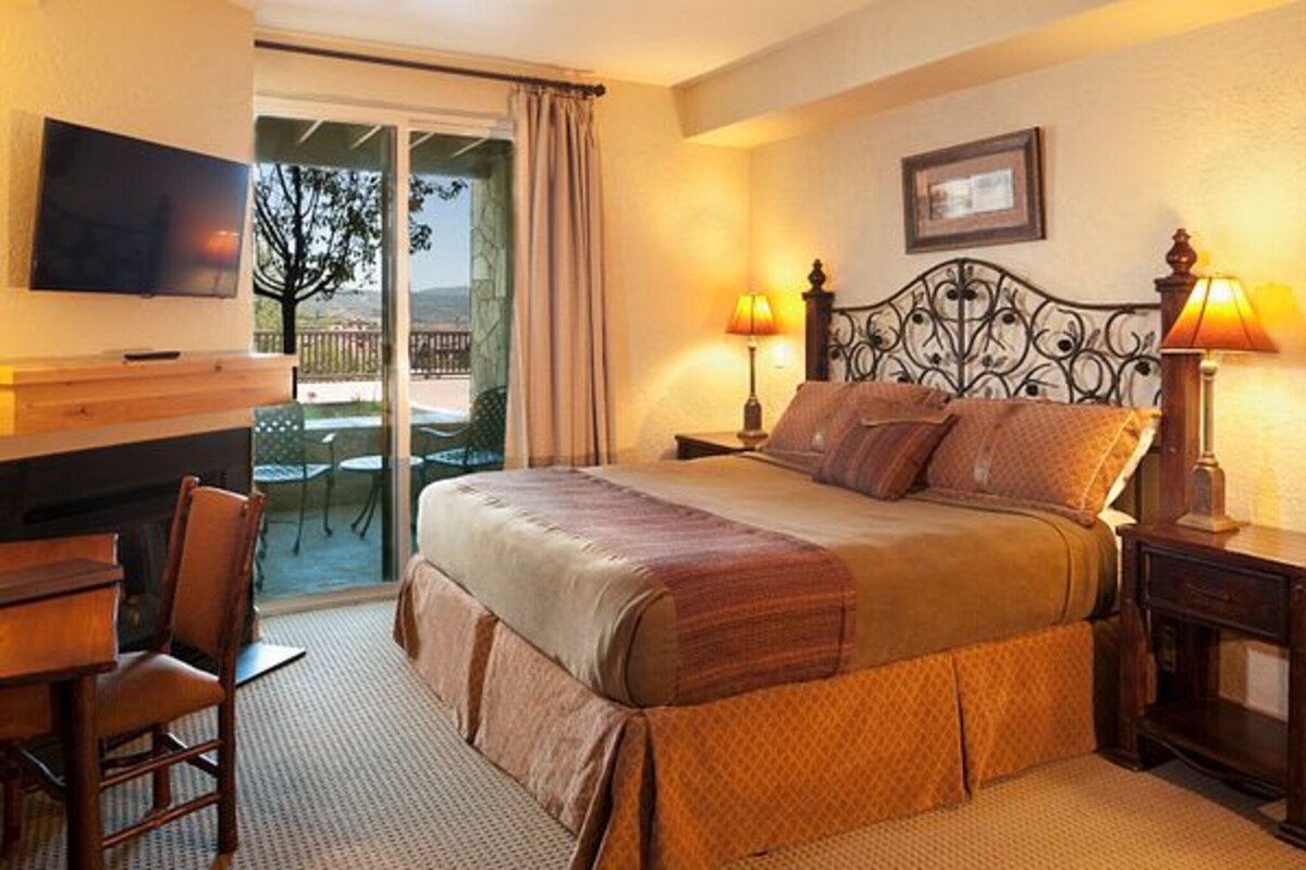 A hotel room with a bed, a TV, a desk with a chair, and a balcony with a view.