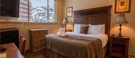 Une chambre d’hôtel équipée d’un lit, de lampes de chevet, d’une télévision, d’une commode et d’une fenêtre donnant sur des immeubles.