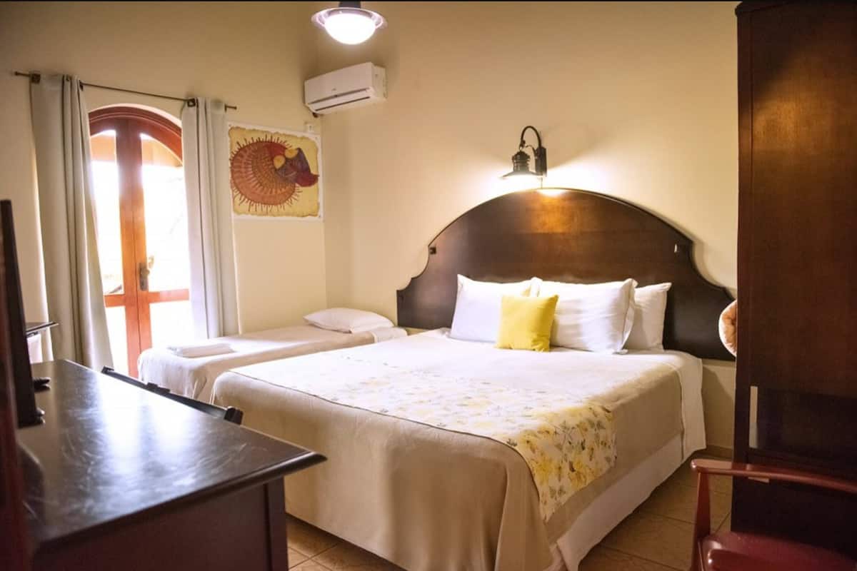 A hotel room with two beds, a wooden headboard, a wall-mounted air conditioner, and a decorative tapestry.
