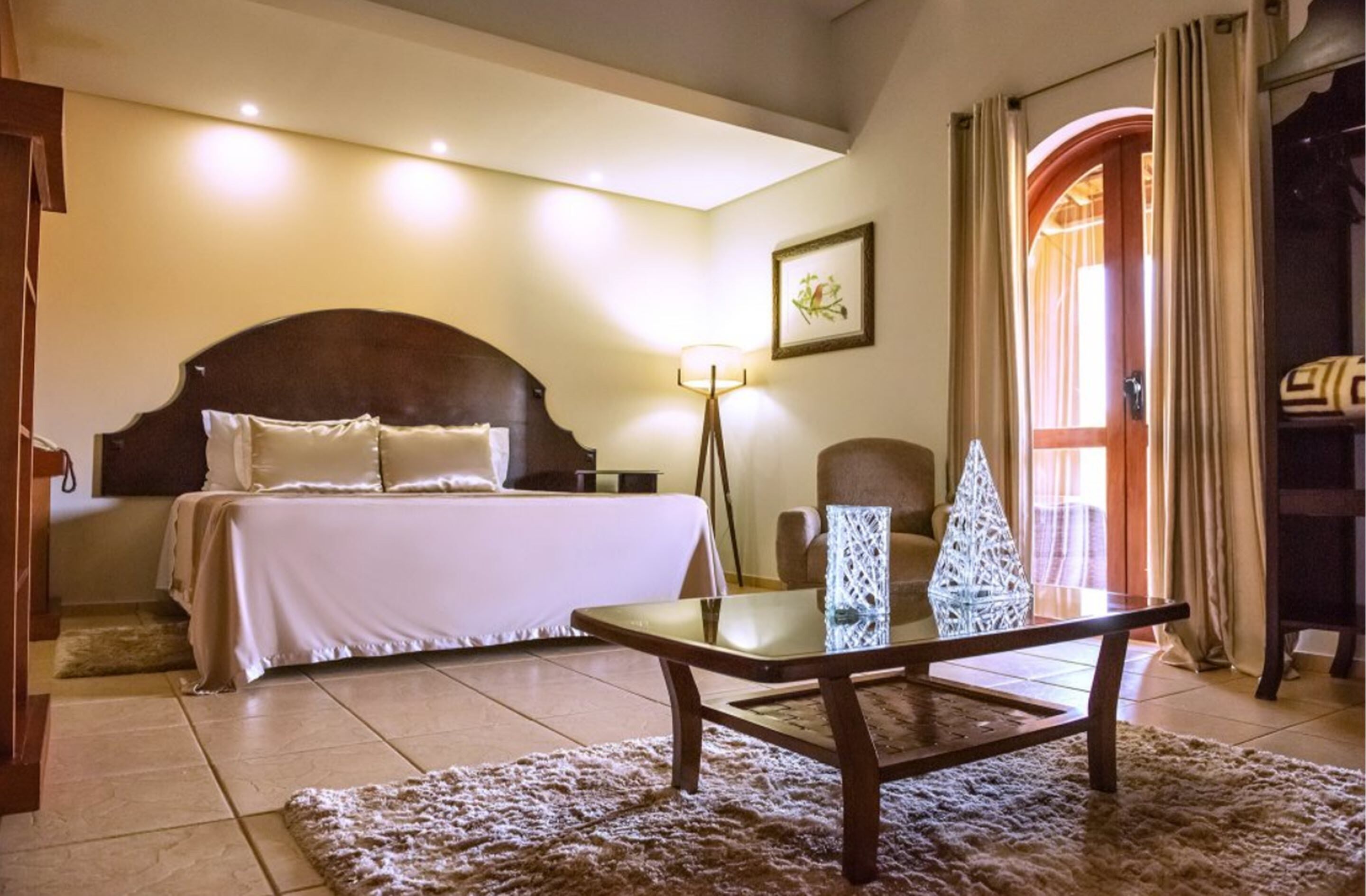 Un dormitorio con cama, mesita de noche, lámpara, sillón y una lámpara de cristal decorativa con forma de árbol.