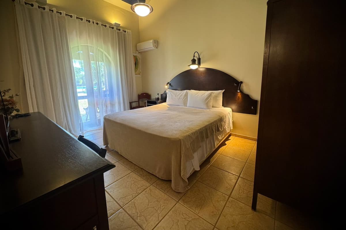 A bedroom with a bed, a desk, an air conditioning unit, and a view of the outdoors.