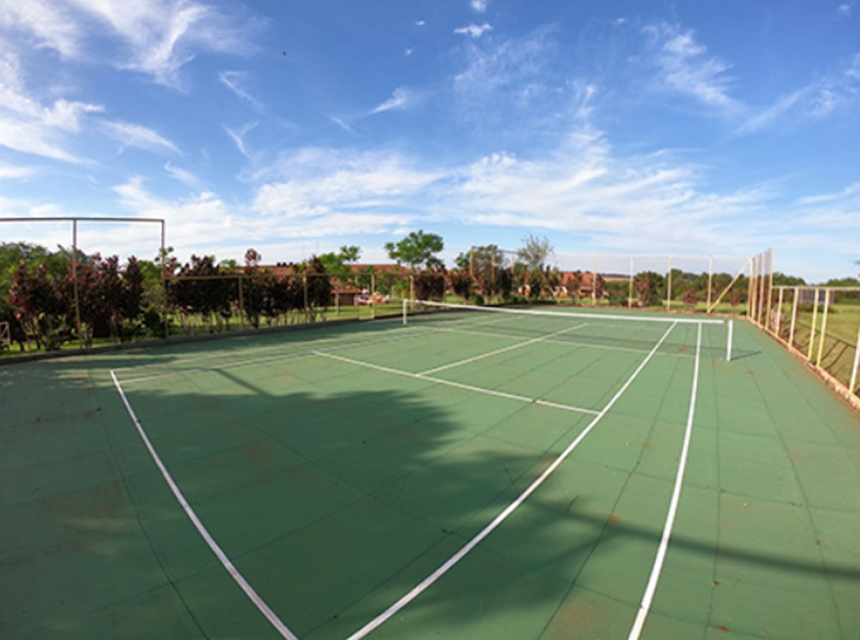 Un court de tennis en plein air, avec un ciel dégagé et des arbres en arrière-plan.