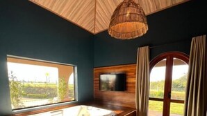 A modern bathroom with a large bathtub, a wooden ceiling, a TV mounted on the wall, and a view of the outdoors through a large window. - Tenonde Park Hotel (Sao Miguel das Missoes)