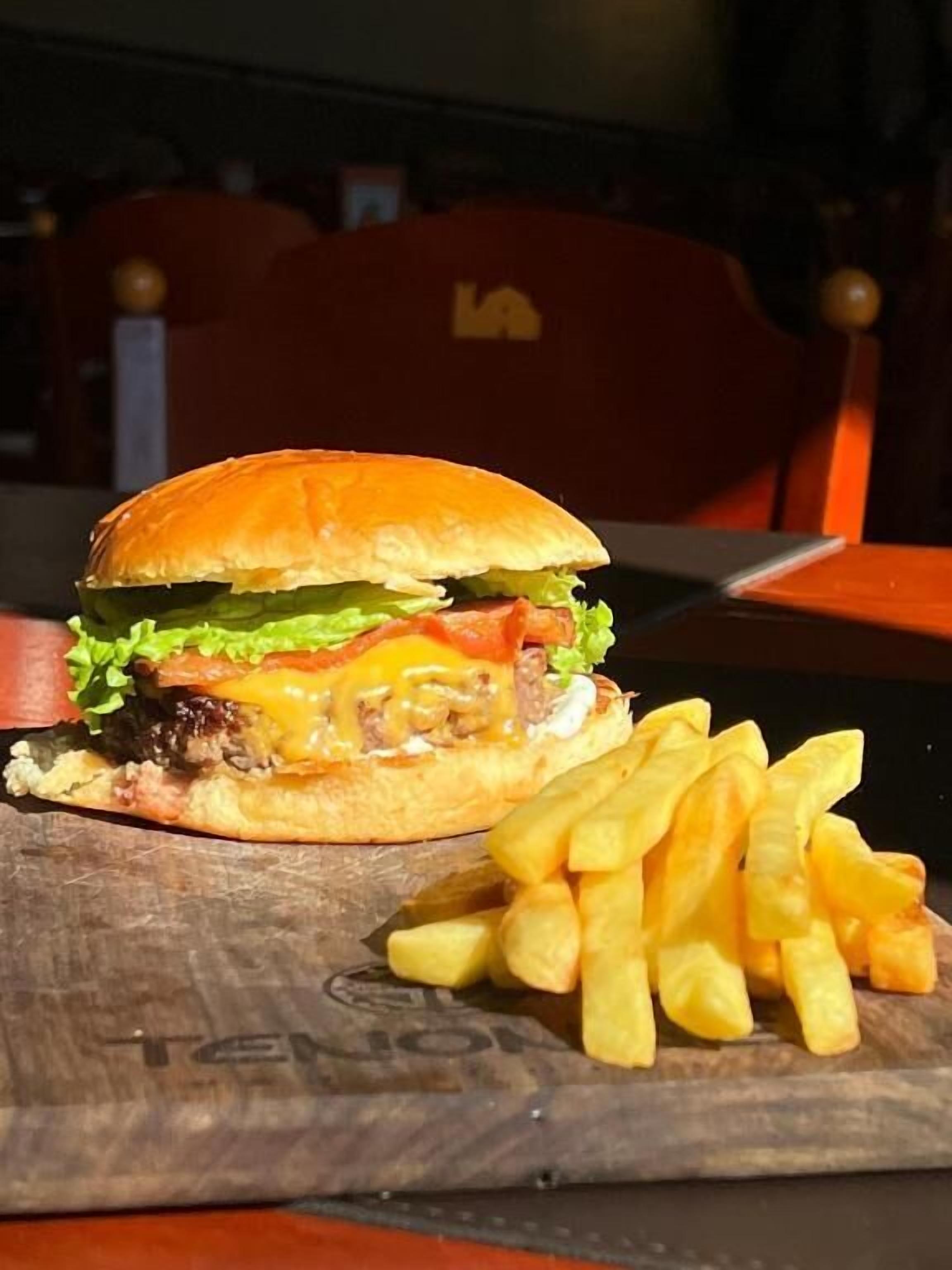 Un hamburger accompagné de frites, le tout servi sur une planche en bois.