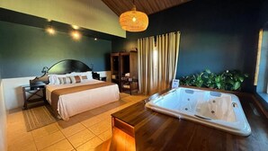 A hotel room with a bed, a wooden side table, a hot tub, and a hanging light fixture. - Tenonde Park Hotel (Sao Miguel das Missoes)