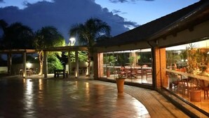 An outdoor patio area with a tiled floor, seating arrangements, and a glass enclosure with tables and chairs. - Tenonde Park Hotel (Sao Miguel das Missoes)