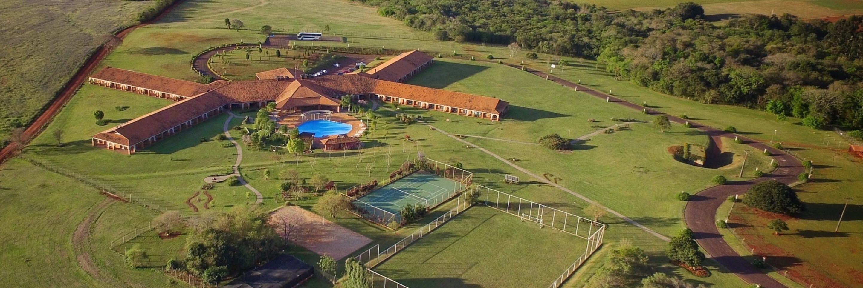 Vista aérea de una extensa propiedad con varias edificaciones, una piscina y amplios campos verdes.