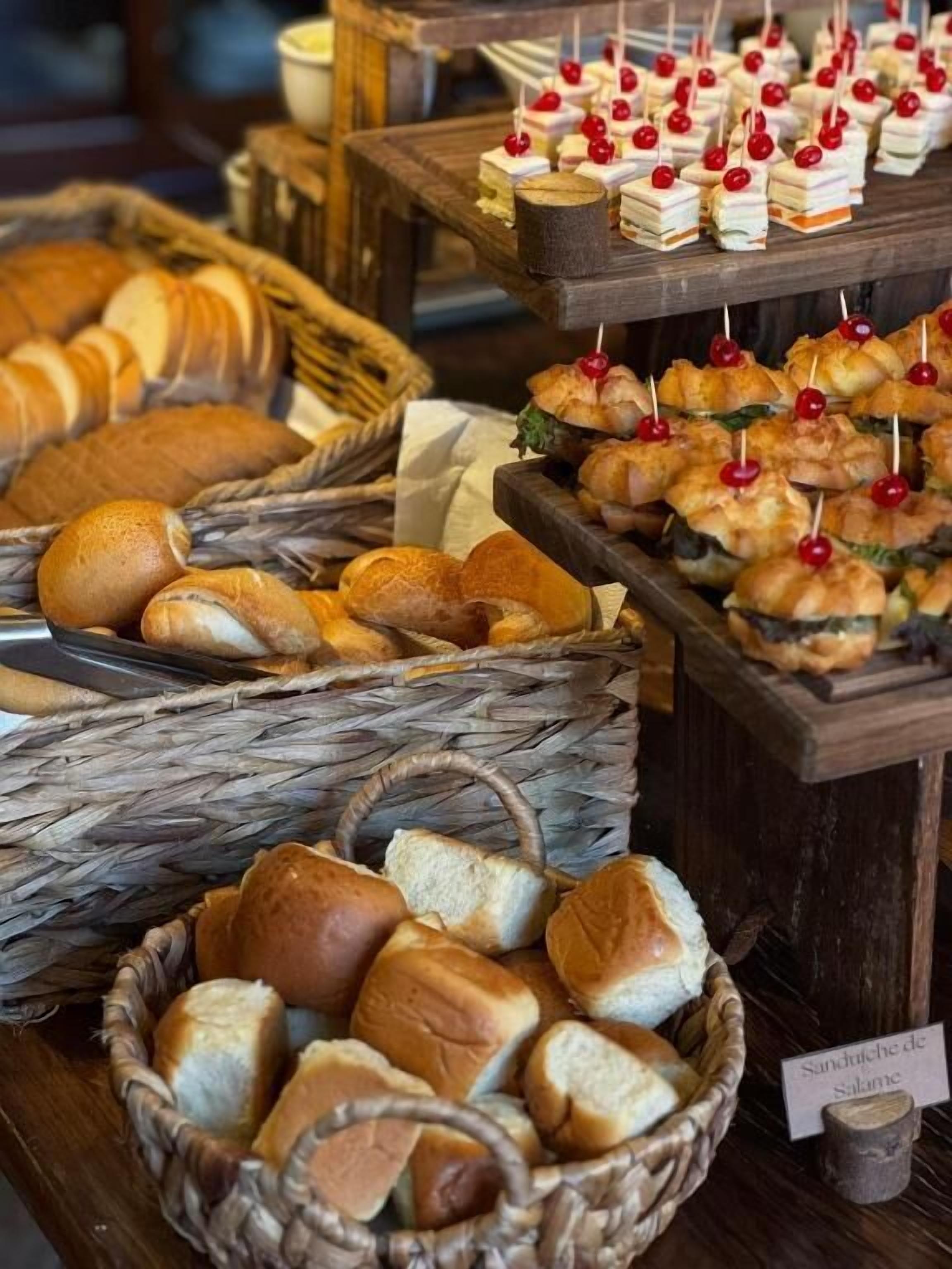 A buffet table with various breads and pastries, including croissants and sandwiches, displayed in baskets and on wooden boards.