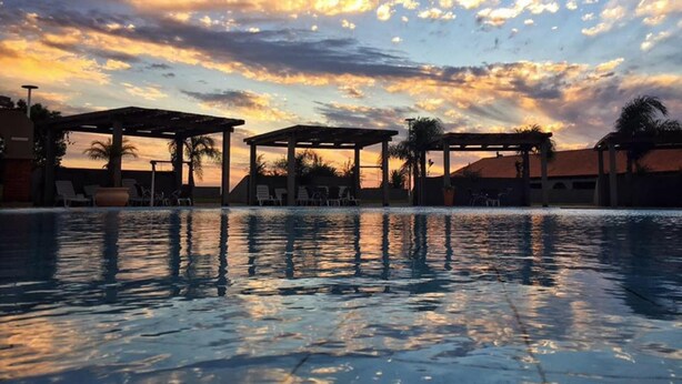 A swimming pool with lounge chairs and umbrellas under a sunset sky. - Tenonde Park Hotel (Sao Miguel das Missoes)