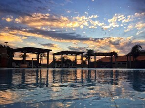 A swimming pool with lounge chairs and umbrellas under a sunset sky.
