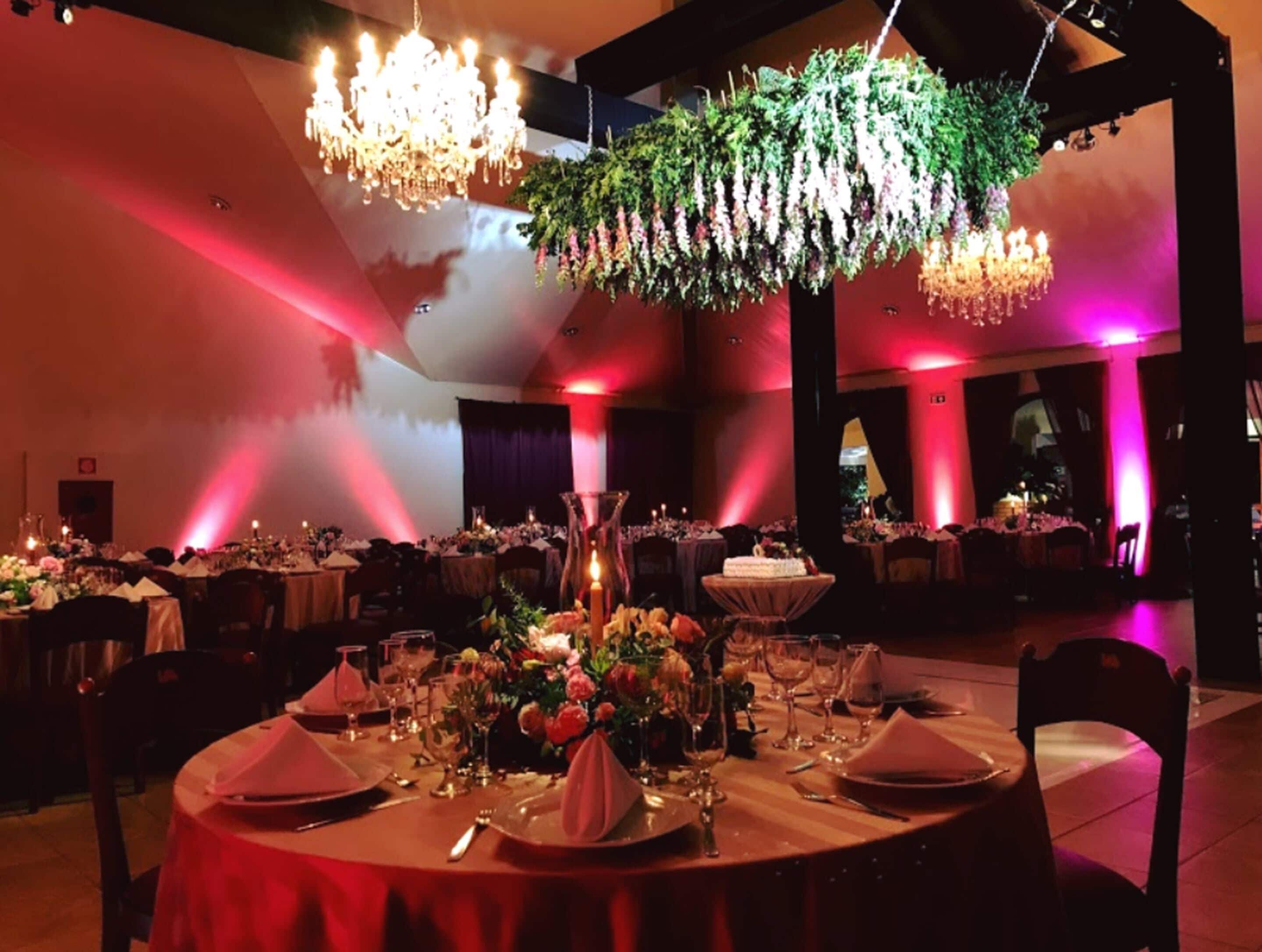 Een balzaal met ronde tafels gedekt voor een formeel evenement, met kroonluchters en bloemstukken als decoratie.