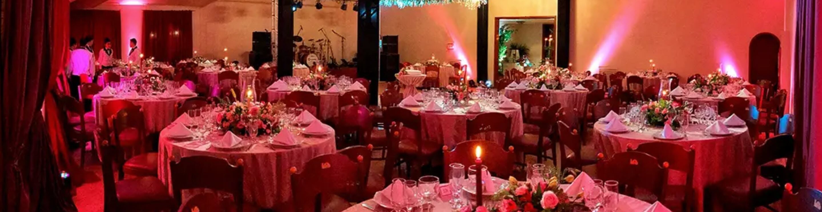 A banquet hall with round tables set for a formal event, featuring floral centerpieces and candlelight.