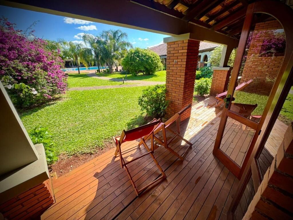 Eine Holzterrasse mit einer Ziegelstütze, einer roten Bank und Blick auf einen gepflegten Rasen und Bäume.