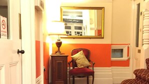 Een hotelkamer met een kamerbreed tapijt, een rode stoel met een gouden kussen, een tafeltje met een lamp en een spiegel aan de muur.