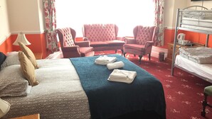 Een hotelkamer met een bed, twee fauteuils, een bank, een televisie en een stapelbed.