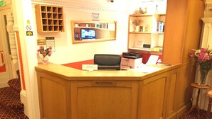 A reception desk with a sign reading "RECEPTION", a television mounted on the wall, and a bookshelf with various items.