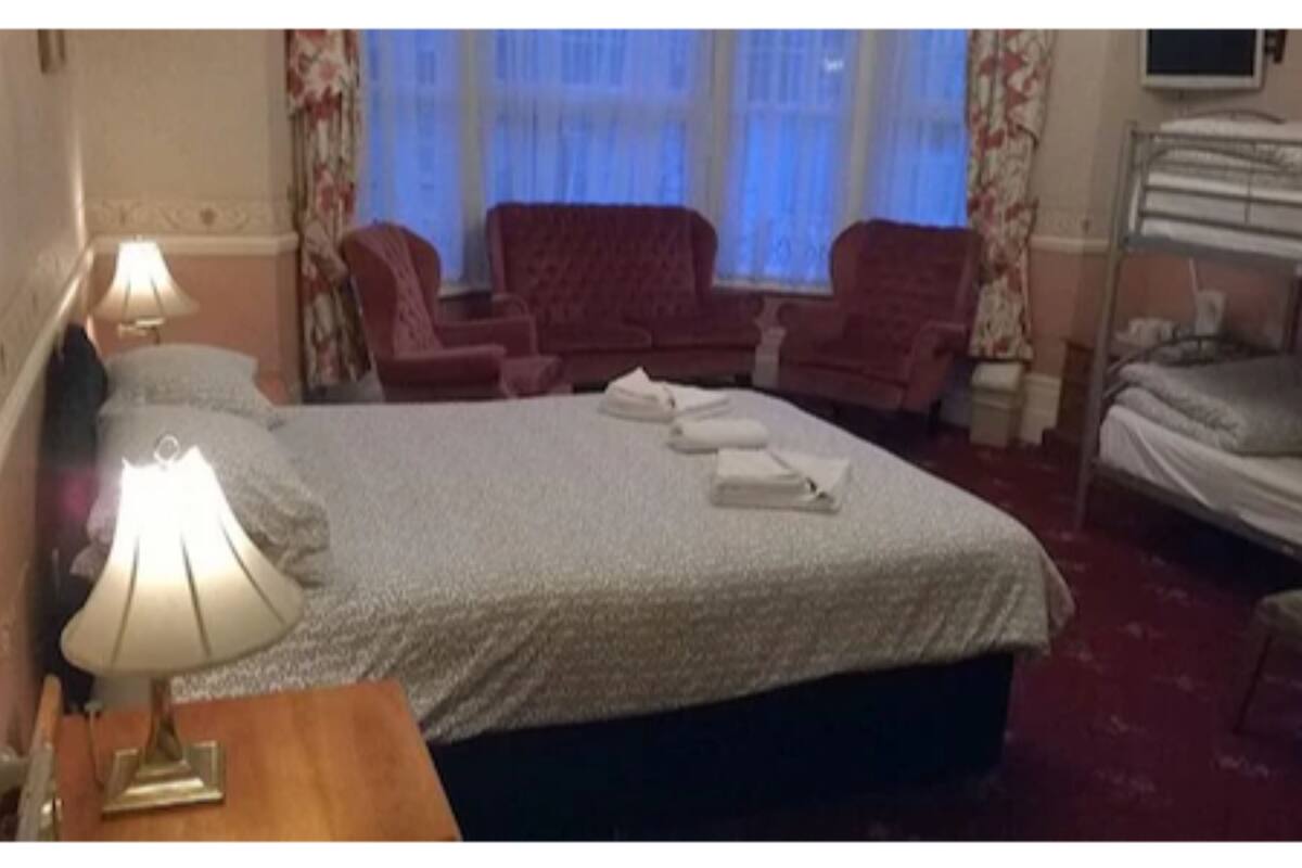 Une chambre d’hôtel avec un lit, un bureau avec une lampe, une chaise, un canapé et un téléviseur.