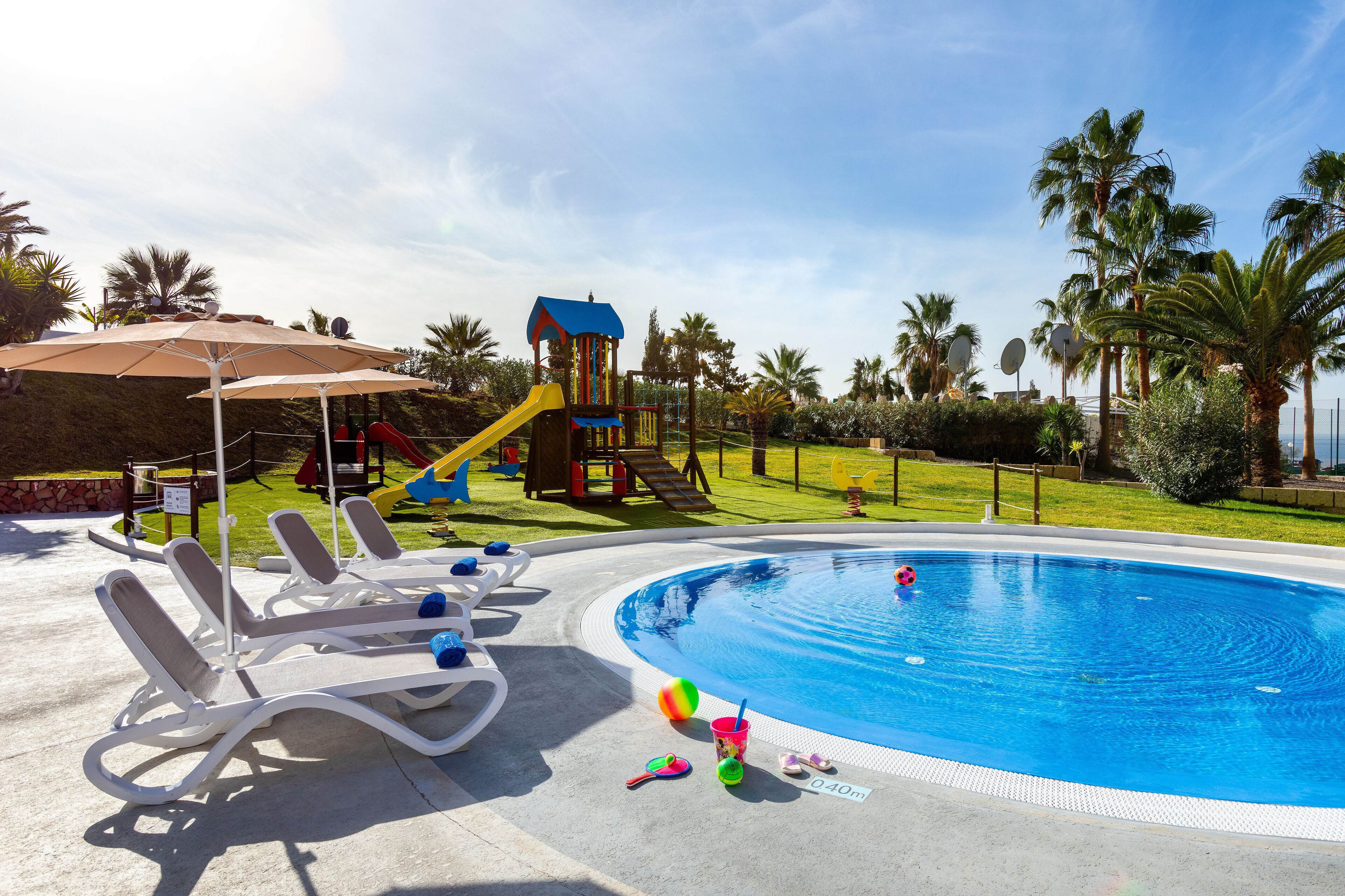 En swimmingpool med solstolar och en lekplats för barn.