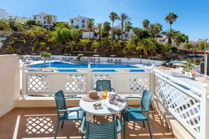 A poolside area with a table and chairs, a pool, and a view of palm trees and buildings in the background. - Hotel Tropical Park (Adeje)