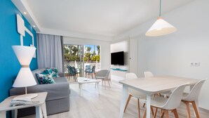 A modern living room with a grey sofa, a white coffee table, and a dining area with a wooden table and white chairs. - Hotel Tropical Park (Adeje)
