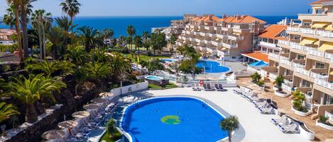 A resort with a large pool, palm trees, and a view of the sea.