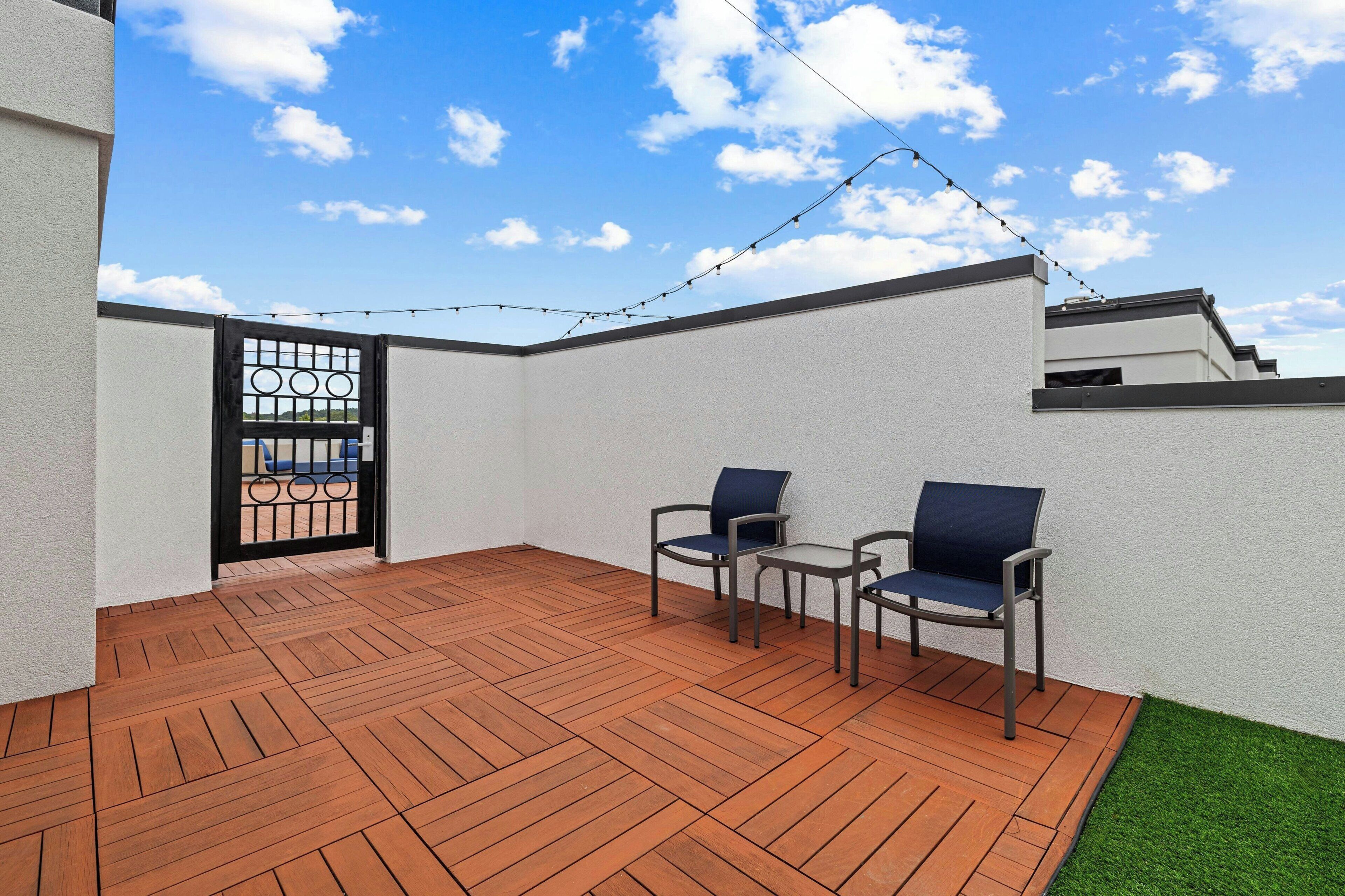 Une terrasse avec un plancher en bois, deux chaises, une petite table et une guirlande lumineuse.