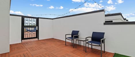 A patio with wooden flooring, two chairs, a small table, and a string of lights.