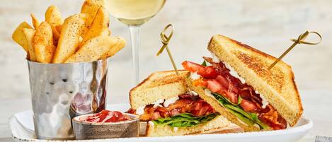 Un sándwich acompañado de papas fritas y una copa de vino blanco sobre un plato.
