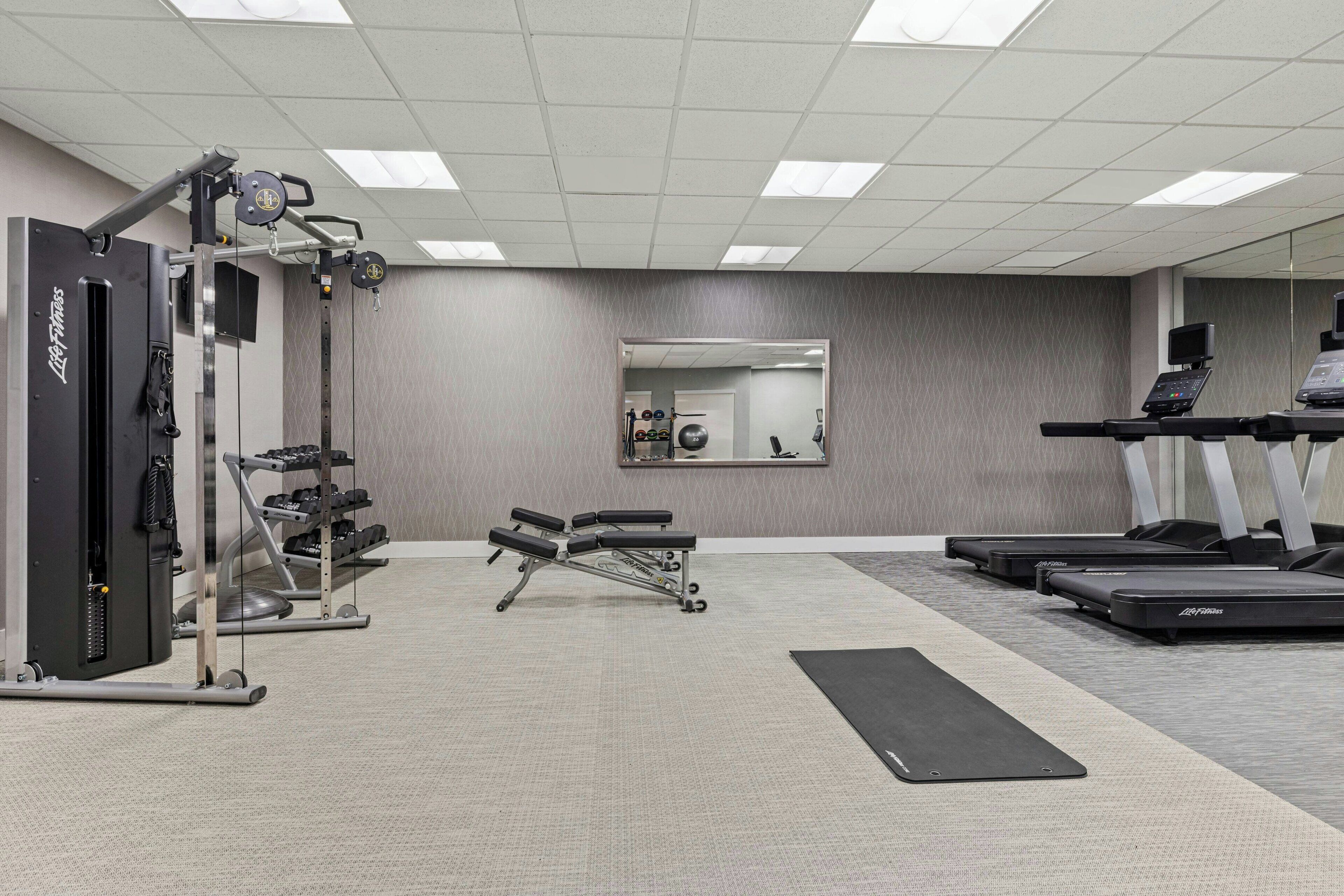 Une salle de sport équipée de machines de cardio, d’appareils de musculation et d’un miroir.