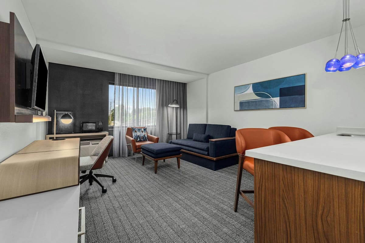 A modern hotel room with a flat-screen TV, a desk, a sofa, and a dining area.