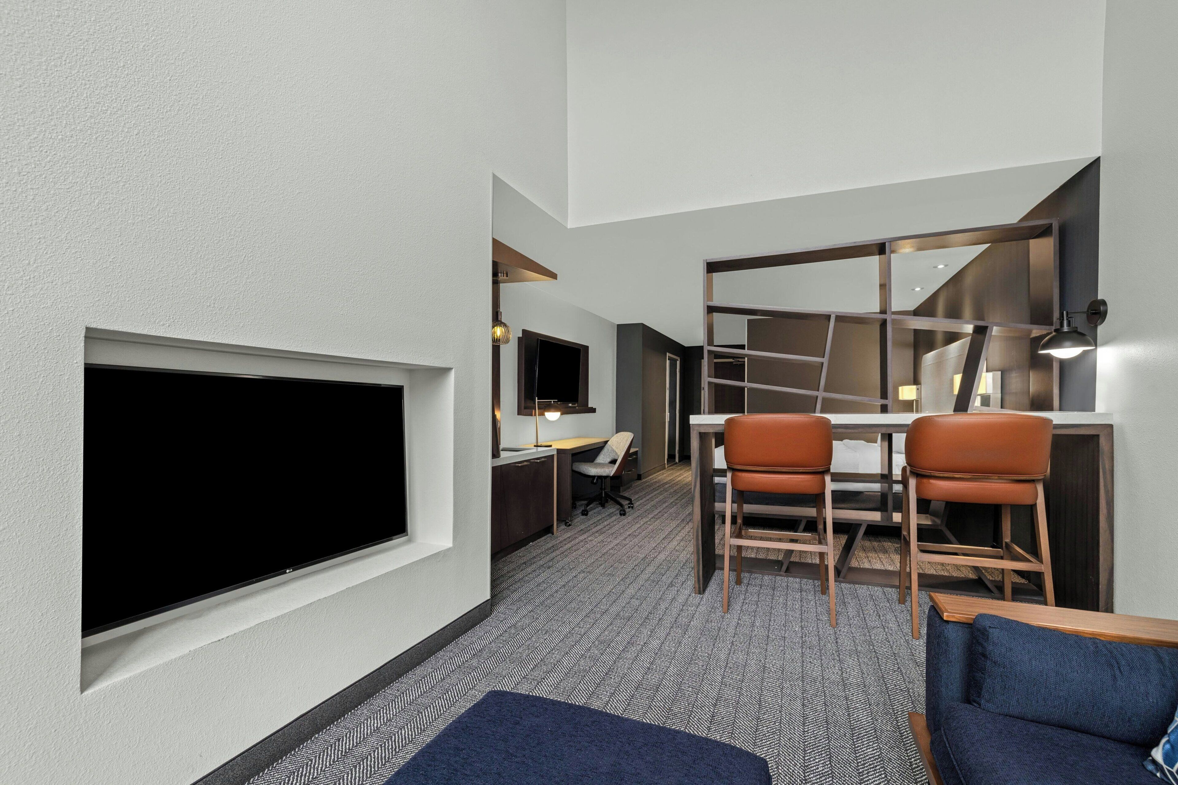 Une chambre d’hôtel dotée d’un grand téléviseur à écran plat, d’un bureau avec deux chaises, d’un canapé et d’un escalier menant à un niveau supérieur.