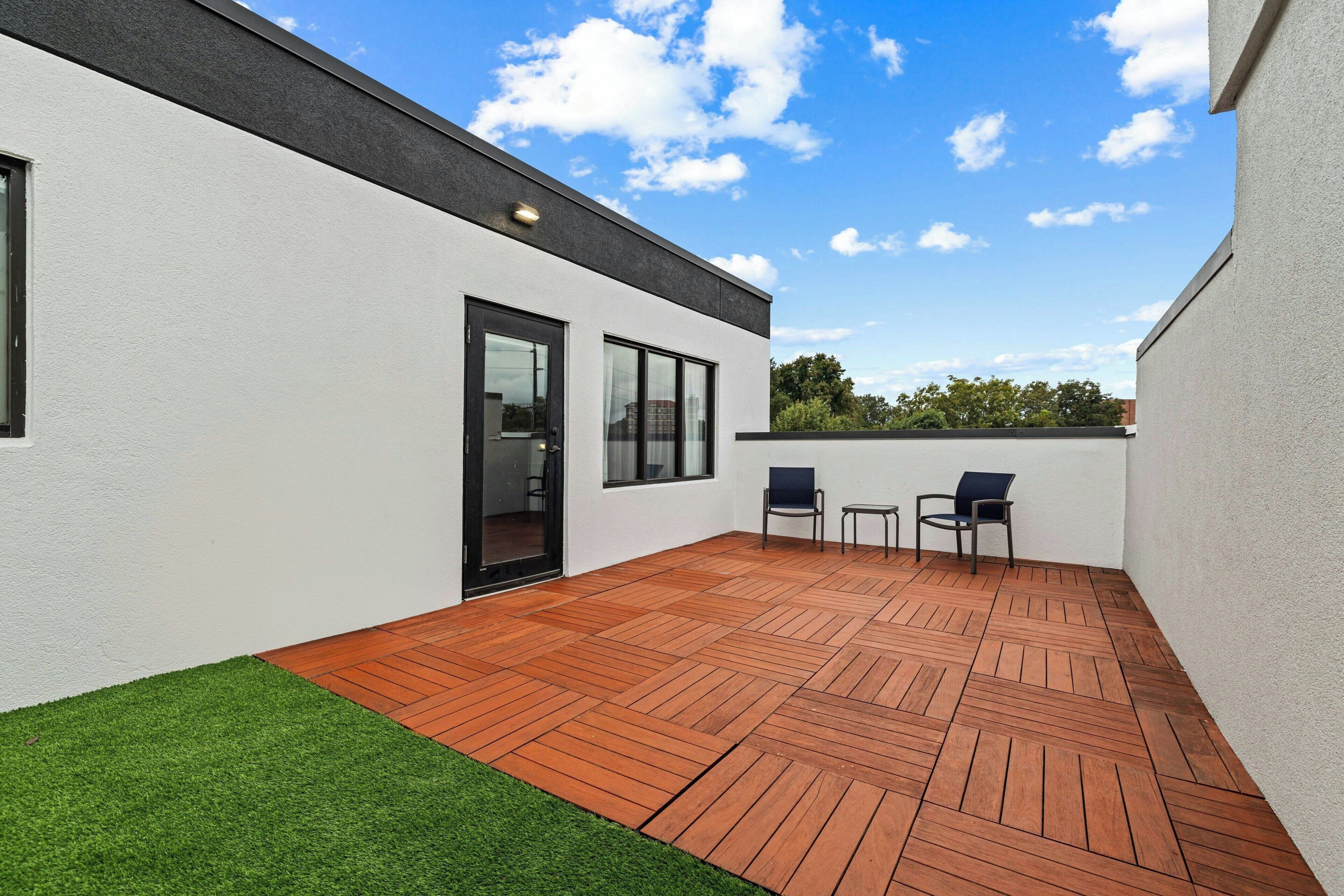 Une terrasse extérieure moderne avec un plancher en bois, deux chaises et une porte vitrée donnant sur un espace intérieur.