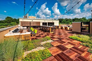 Um pátio externo com um deck de madeira, áreas de estar e luzes de corda.