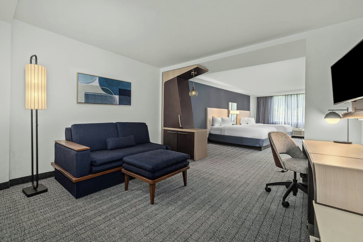 A modern hotel room with a sofa, ottoman, desk, and a bed.