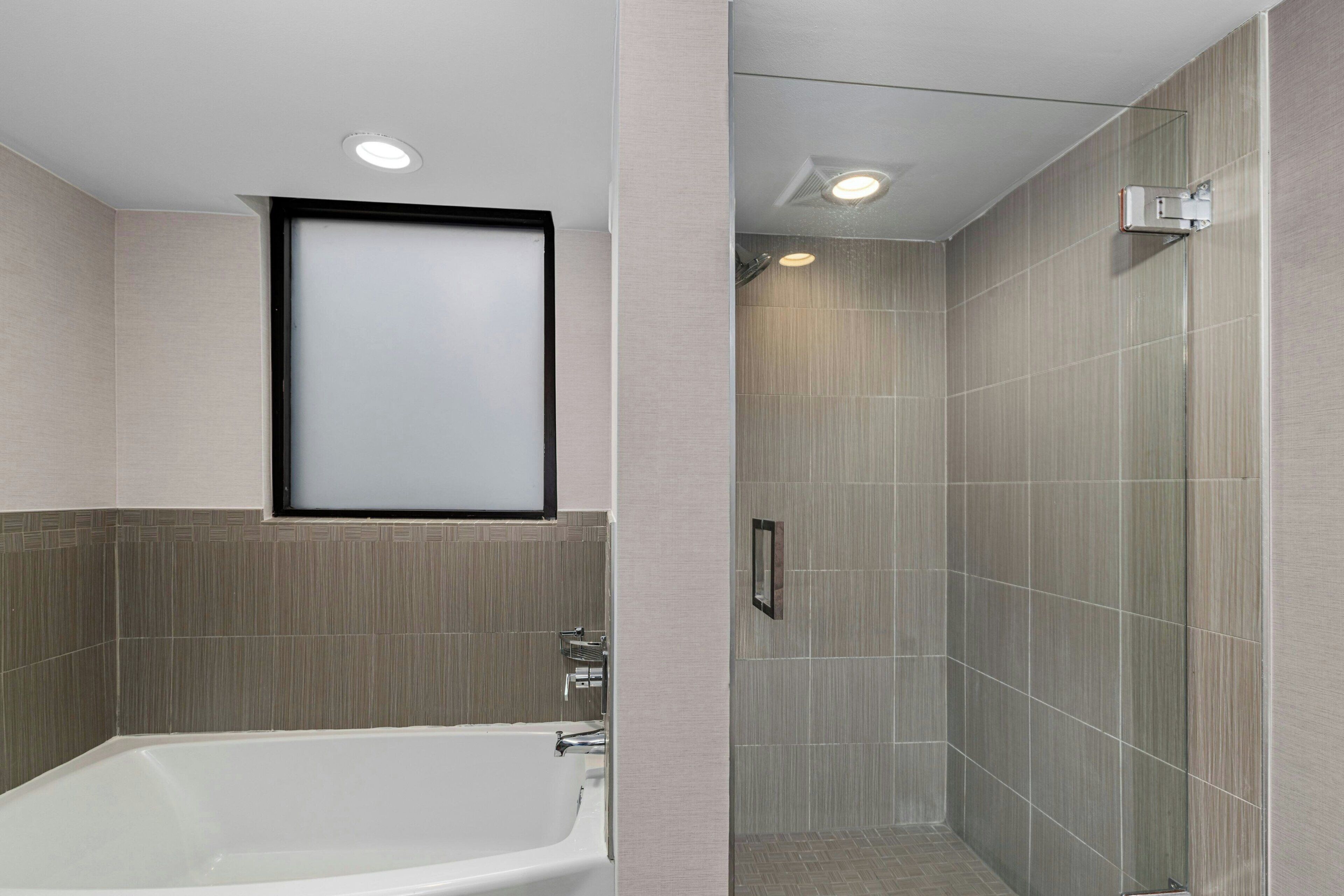 A modern bathroom with a bathtub, shower, and tiled walls.