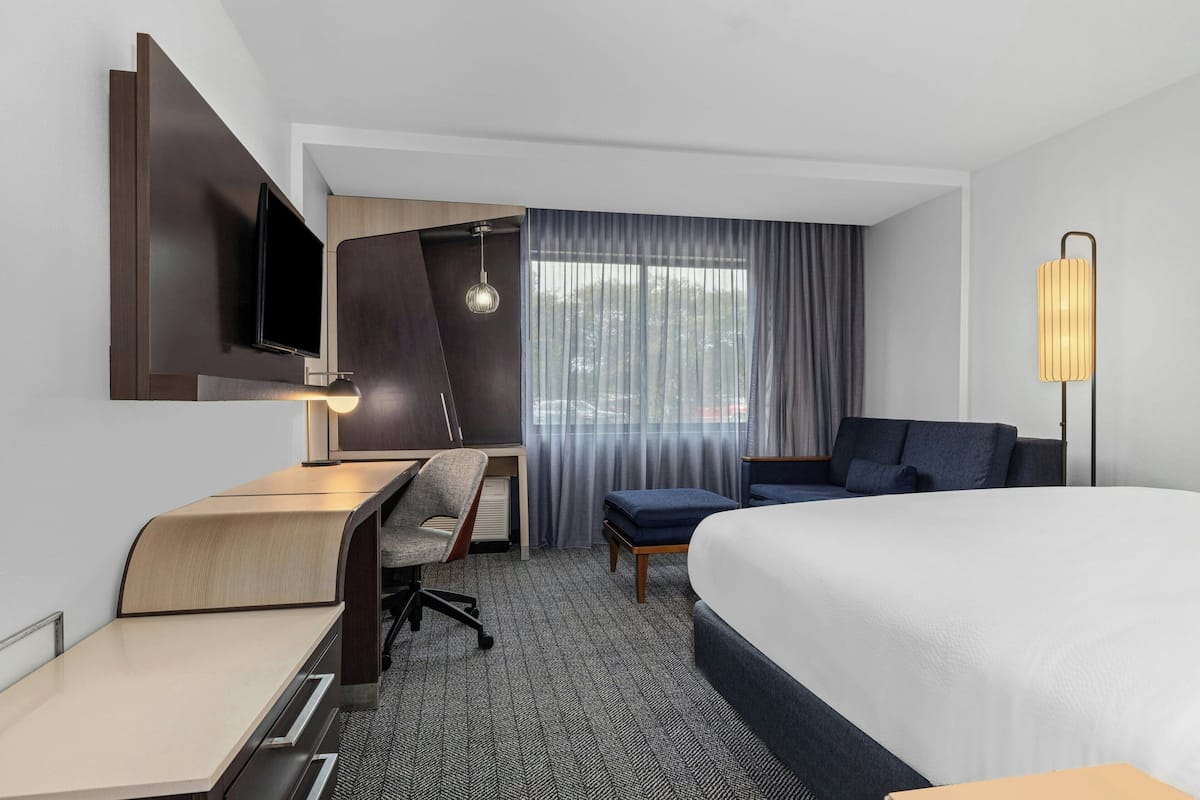 A modern hotel room with a bed, desk, chair, and a TV mounted on the wall.