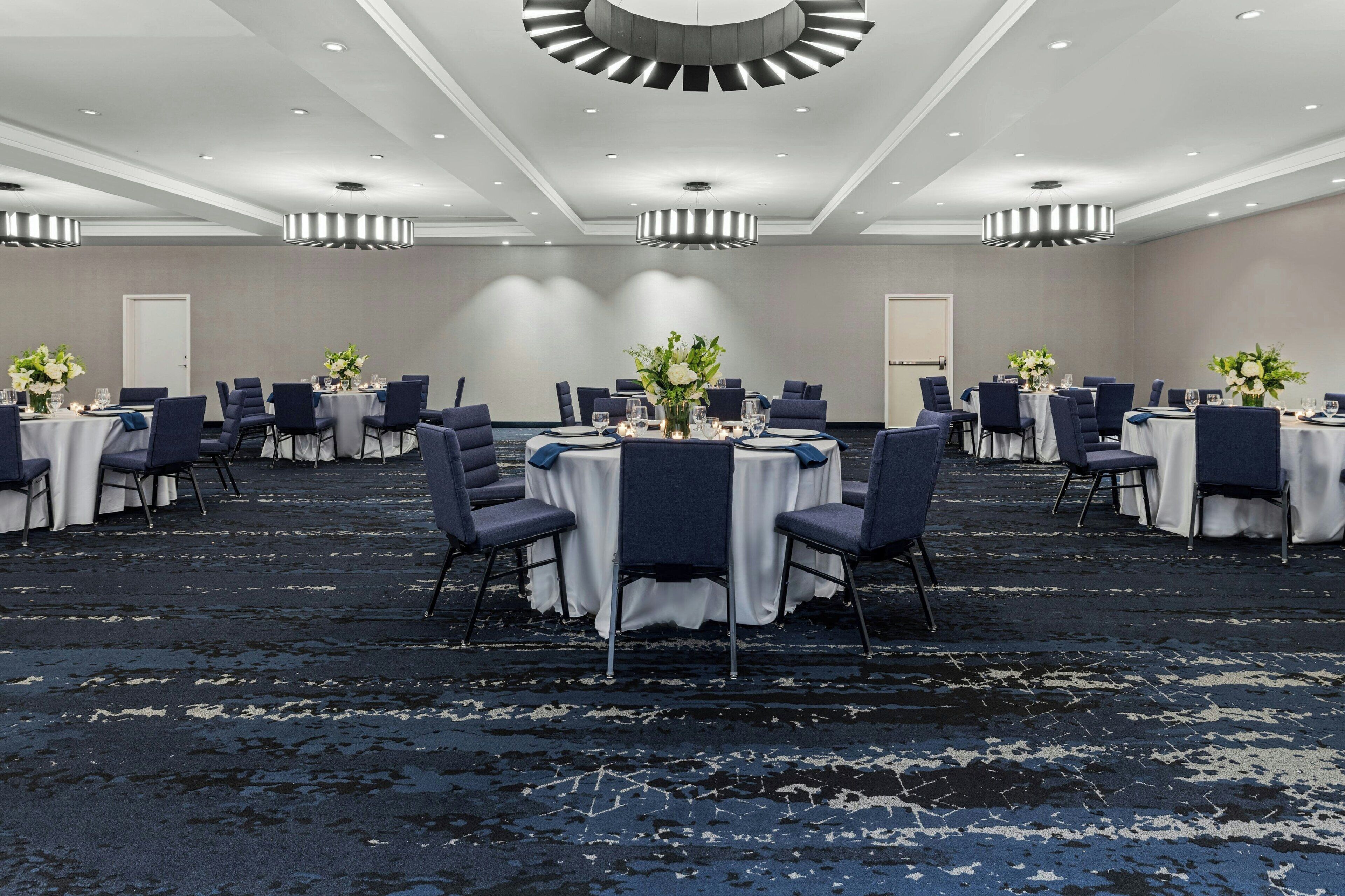Un salón de conferencias con mesas redondas, sillas y centros de mesa florales.