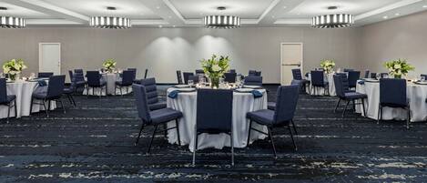 Un salón de conferencias con mesas redondas, sillas y centros de mesa florales.