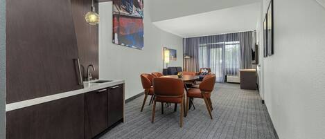 Une chambre d’hôtel moderne avec des finitions en bois foncé, un coin repas avec des chaises orange et une grande fenêtre avec des rideaux.