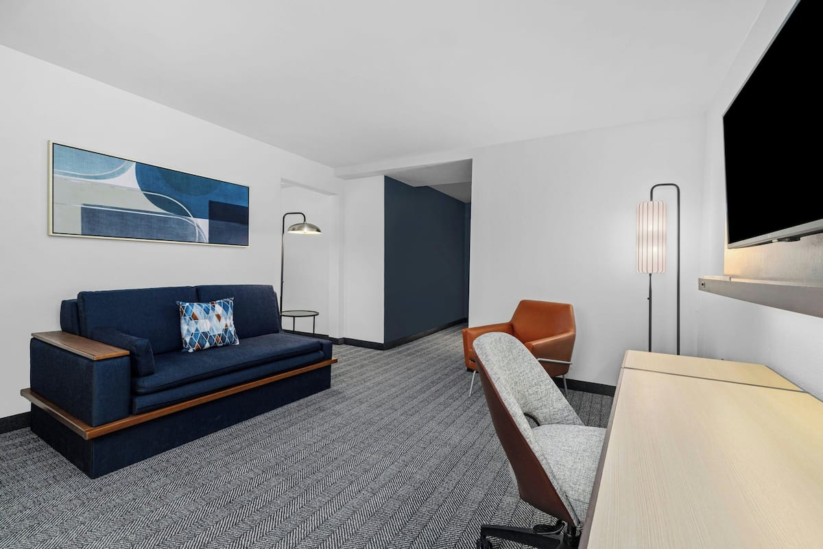 A modern hotel room with a sofa, armchair, and a flat-screen TV.