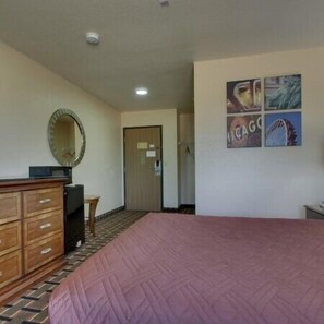 A hotel room with a bed, a wooden dresser, a small table, a mirror, and a wall with four framed pictures. - Heritage Grand Inn (Canton)