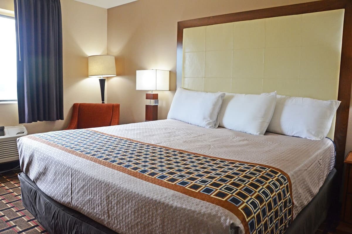 A hotel room with a large bed, two bedside lamps, a chair, and an air conditioning unit.