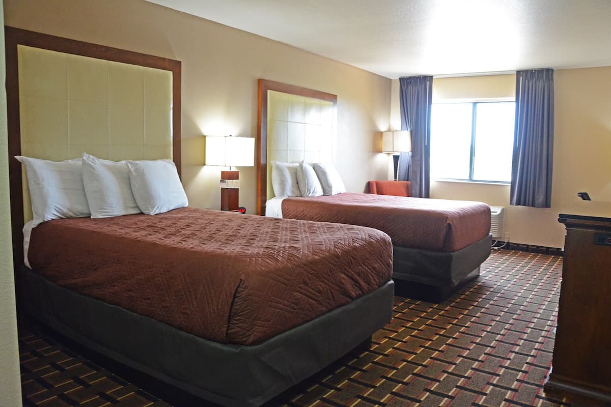 A hotel room with two beds, a large mirror, a desk, and a window with curtains.